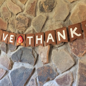 May include: A brown felt banner with white letters spelling "GIVE THANKS" and a small felt turkey in the middle.