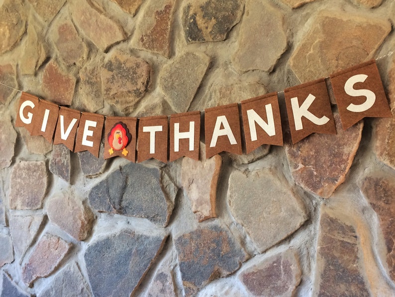 May include: A brown felt banner with white letters spelling "GIVE THANKS" and a small felt turkey in the middle.
