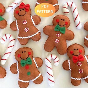 May include: A collection of brown felt gingerbread people ornaments with embroidered faces, red cheeks, and white icing details. Some figures wear green or red felt bows or scarves. White and red striped felt candy canes are interspersed throughout.