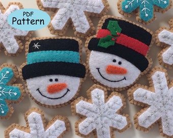 May include: A set of felt ornaments featuring two snowmen with black hats and white faces, and five snowflakes with silver glitter. The ornaments are brown with a white outline. The text "PDF Pattern" is written in a blue oval.