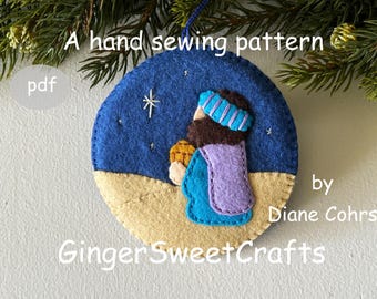 May include: A circular felt ornament featuring a hand-sewn scene of a figure in a blue and purple robe against a dark blue night sky with a star. The text reads: A hand sewing pattern pdf by Diane Cohrs GingerSweetCrafts.