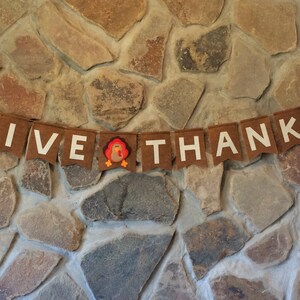 May include: A brown felt banner with white letters that reads "GIVE THANKS" with a small felt turkey in the middle.