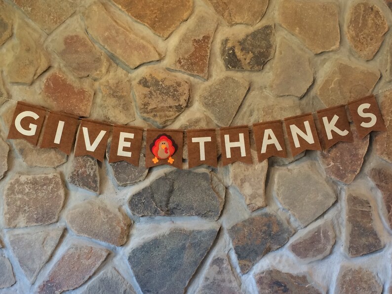 May include: A brown felt banner with white letters that reads "GIVE THANKS" with a small felt turkey in the middle.