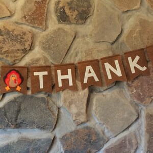 May include: A brown felt banner with white letters spelling "Give Thanks" and a felt turkey in the middle.