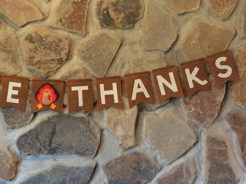 May include: A brown felt banner with white letters spelling "Give Thanks" and a felt turkey in the middle.