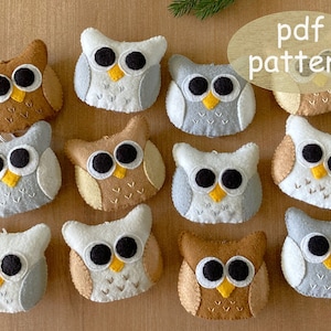 May include: A set of 10 felt owl ornaments in various colors, including brown, beige, gray, and white. The owls have black eyes, yellow beaks, and white felt accents. The owls are arranged in a circle on a wooden surface. The text "pdf pattern" is written in a yellow circle on the top right of the image.