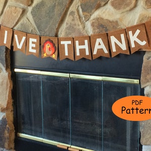 May include: A brown felt banner with white letters that reads "GIVE THANKS" with a felt turkey applique in the middle. The banner is hanging above a fireplace.