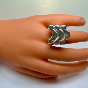 May include: A silver ring with a geometric design. The ring is made of three interlocking pieces that form a wave-like pattern.