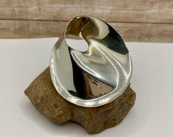 May include: A silver, abstract, wavy, organic shaped brooch. The brooch is smooth and shiny.