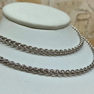May include: Two silver chains, one on top of the other, on a white display stand. The chains are made of a twisted rope design.