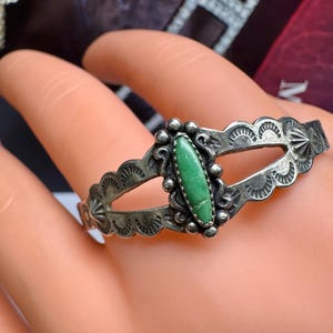 Puede incluir: Un brazalete de plata con una piedra turquesa verde engastada en un diseño decorativo. El brazalete tiene un diseño de corte y está hecho en estilo nativo americano.