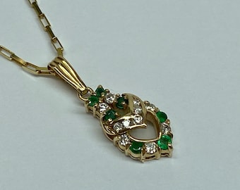 Puede incluir: Un collar de cadena de oro con un colgante con un diseño en forma de corazón con piedras de esmeralda y diamante.