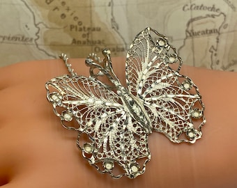 May include: A silver filigree butterfly pendant necklace. The butterfly is detailed with a delicate, intricate design and has small clear stones on the wings.