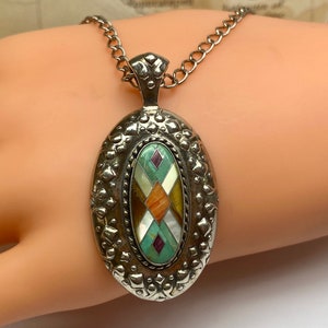 May include: A silver oval pendant necklace with a multi-coloured stone inlay. The stone is a geometric pattern of turquoise, brown, white, and purple.