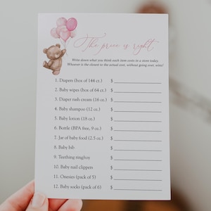 May include: A baby shower game card with the text "The price is right." The card features a watercolor illustration of a teddy bear holding pink balloons. The card lists baby items with blank spaces for prices.