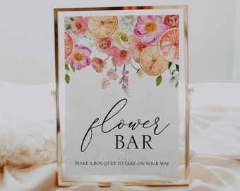 Pode incluir: Uma placa branca com moldura dourada e um desenho floral com flores cor-de-rosa e fatias de citrinos laranja. A placa diz "flower bar" e "make a bouquet to take on your way".