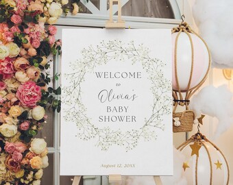 Puede incluir: Un letrero blanco sobre un caballete de madera con el texto "WELCOME to Olivia's BABY SHOWER" rodeado por una corona floral. La fecha "August 12, 20XX" está impresa debajo. Globos aerostáticos decorativos y arreglos florales en el fondo.