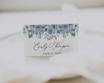 Può includere: Un segnaposto bianco con un design floreale blu e il testo "Everly Thompson" e "Tavolo Uno".
