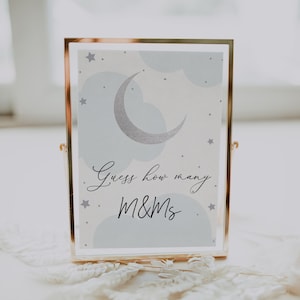 May include: A gold-framed sign with a blue and white moon and stars design. The sign says "Guess how many M&Ms".
