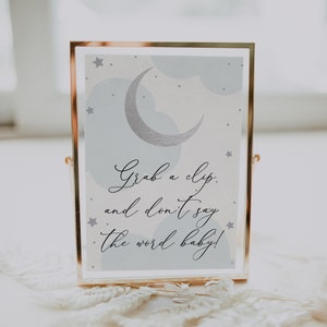 Può includere: Un cartello con cornice dorata con sfondo blu e bianco che presenta una luna crescente e stelle. Il cartello dice "Grab a clip and don't say the word baby!"