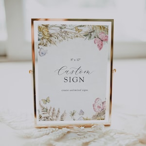 May include: A gold-framed sign with a white background and a floral border. The sign says "Custom SIGN create unlimited signs" and has the dimensions "8" x 10".