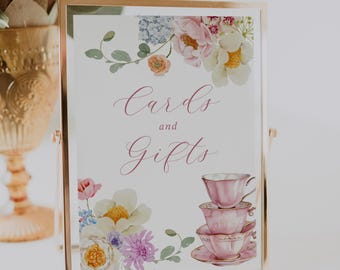May include: A white sign with a pink floral border and a pink teacup stack. The sign says "Cards and Gifts" in pink cursive.