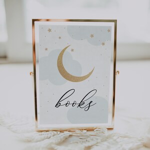 Puede incluir: Una imagen enmarcada en oro con un fondo azul y una luna creciente dorada con estrellas. El texto "libros" está escrito en letras cursivas negras.