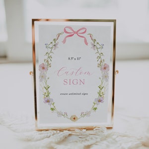 May include: A gold-framed sign with a floral wreath design and a pink ribbon. The sign reads "8.5" x 11" Custom Sign create unlimited signs".