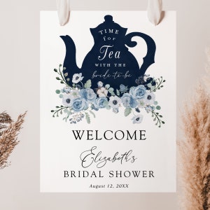 May include: A white welcome sign with a blue teapot silhouette and blue floral accents. The text reads "Time for Tea with the bride-to-be" and "Welcome Elizabeth's Bridal Shower August 12, 20XX".