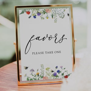 Puede incluir: Un cartel con marco dorado, fondo blanco y borde floral. El cartel dice "favors" en letra cursiva y "Please take one" en una fuente más pequeña.