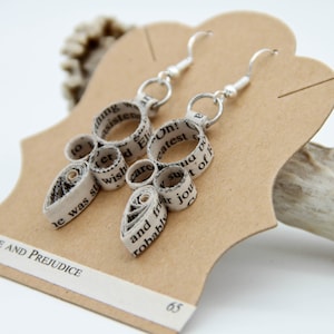 May include: A pair of dangle earrings crafted from rolled paper strips featuring printed text from the book Pride and Prejudice. The earrings consist of circular and teardrop-shaped paper coils attached to silver-toned metal hooks.