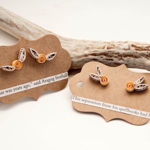 May include: Handmade paper earrings with a floral design in shades of orange and cream, displayed on decorative brown tags with text. The earrings are set against a white background with a deer antler.