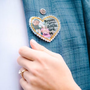 Può includere: Un cerotto di stoffa a forma di cuore con una foto di un uomo e una bambina. Il cerotto è ricamato con il testo "Forever your little girl 1-20-24".