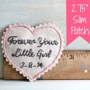 Puede incluir: Un parche bordado en forma de corazón de 2,75 pulgadas con puntadas rosas. El parche está hecho de tela beige y presenta el texto "Forever Your Little Girl 3-8-14".