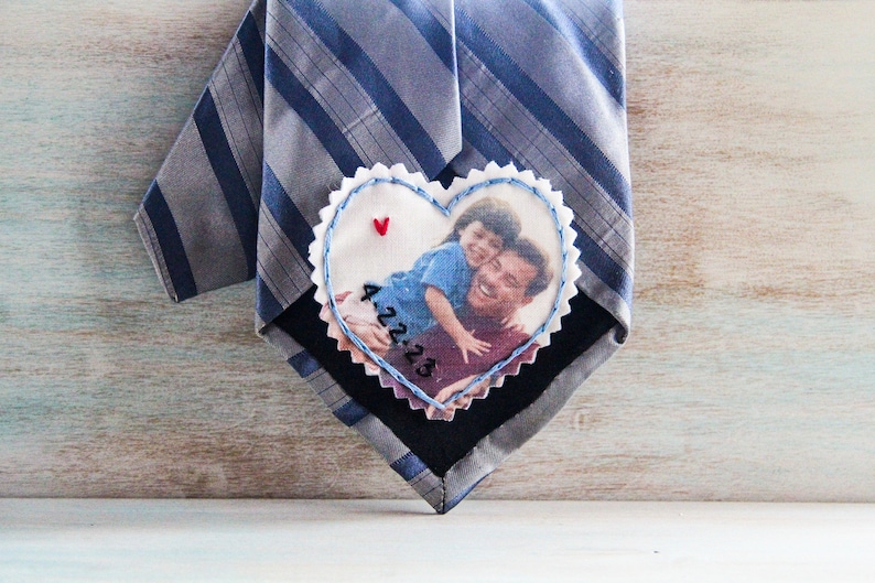 May include: A heart-shaped fabric patch with a photo of a father and child. The patch is sewn onto a striped tie. The date "4.22.13" is embroidered on the patch.