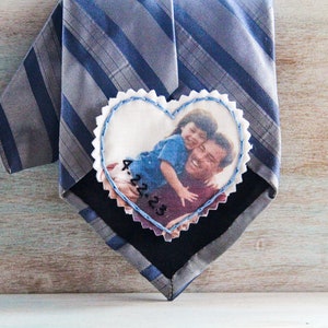 May include: A heart-shaped fabric patch with a photo of a father and child. The patch is attached to a striped tie. The date "4.22.23" is embroidered on the patch.
