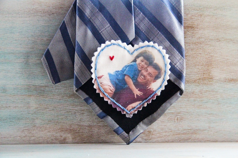 May include: A heart-shaped fabric patch with a photo of a father and daughter. The patch is attached to a striped tie.