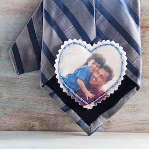 May include: A gray and blue striped tie with a heart-shaped fabric patch sewn on. The patch has a photo of a father and child smiling.