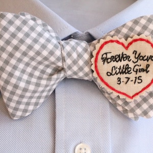 Puede incluir: Una pajarita de cuadros vichy gris y blanco con un parche beige en forma de corazón que dice "Forever Your Little Girl 3-7-15" en cursiva negra.