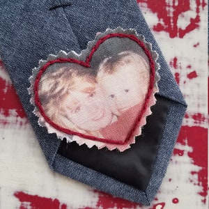 May include: A blue tie with a red heart-shaped patch sewn on. The patch has a photo of two people inside.