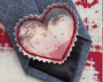 May include: A blue tie with a red heart-shaped patch sewn on. The patch has a photo of two people inside.