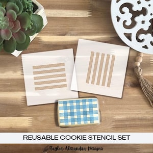 May include: A reusable cookie stencil set with three designs: horizontal stripes, vertical stripes, and a plaid pattern. The stencils are white, and the cookie has a blue and white plaid design. The text "REUSABLE COOKIE STENCIL SET" is at the bottom.