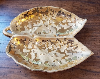 May include: A gold leaf-shaped ceramic dish with a textured surface. The dish has a handle on one side and is perfect for serving snacks or holding jewelry.