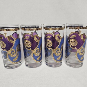 May include: Set of four clear glass tumblers with a gold and purple abstract design. The glasses have a rounded bottom and a straight top.