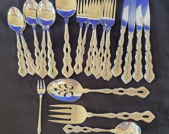 May include: A set of silverware with ornate handles. The set includes spoons, forks, knives, a serving spoon, a serving fork, and a butter knife. The silverware is made of polished stainless steel.