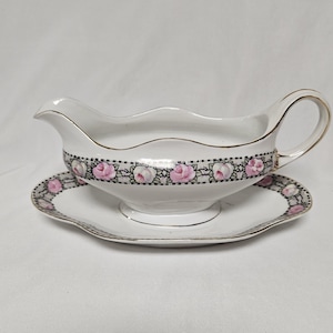 May include: White porcelain gravy boat with a pink and black floral design and a matching saucer.
