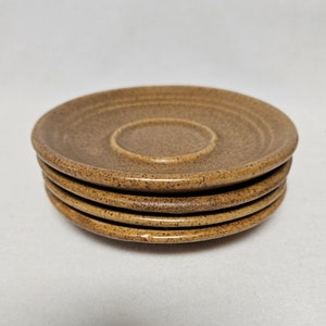 May include: A stack of four brown ceramic saucers with a slightly raised centre. The saucers are speckled with a lighter brown colour.