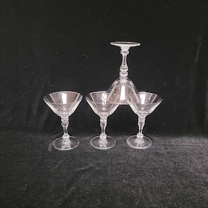 May include: Four clear glass cocktail glasses, three are martini glasses and one is a coupe glass. The coupe glass is upside down on top of the three martini glasses.