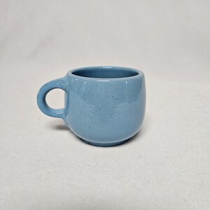 Op de afbeelding: Een lichtblauwe keramische mok met een afgeronde vorm en een handvat.