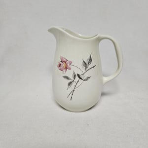 May include: White ceramic jug with a pink rose and grey leaves design.